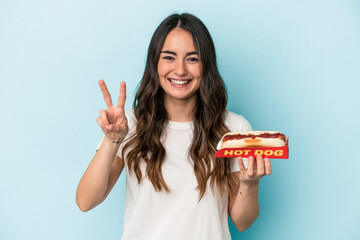 Young caucasian woman holding a hot dog isolated on blue background showing number two with fingers.