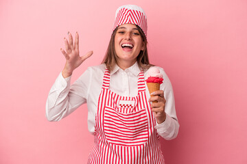 Wall Mural - Young ice cream maker woman holding ice cream isolated on pink background receiving a pleasant surprise, excited and raising hands.