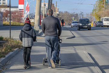 A father walks with two children on the sidewalk on a sunny autumn day