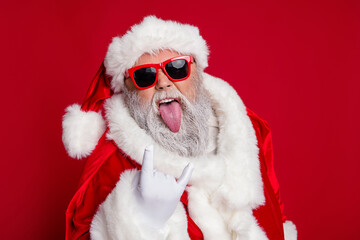 Poster - Photo of cool funky santa claus wear red costume hat dark eyewear showing hard rock sign tongue isolated red color background