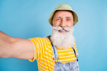 Sticker - Photo of optimistic old white beard man do selfie wear cap yellow t-shirt overall isolated on blue color background