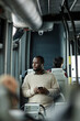 Vertical portrait of African-American man looking at window in bus while traveling by public transport in city