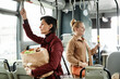 Side view portrait of woman holding grocery bag on bus while traveling by public transport and holding onto railing, copy space