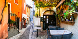 Fototapeta Uliczki - Charming old narrown streets of Italian villages. Malcesine, Garda lake, Italy. Autumn colors, cosy street bars