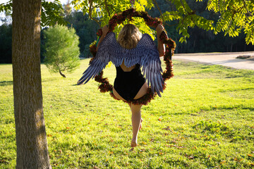 adult woman with blonde hair and a bit chubby doing physical exercise in the park on an acrobatic hoop. The woman is wearing black lingerie and black Halloween wings. Outdoor sport and health concept