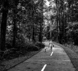 mature outgoing woman walking her dog through woods on paved LINC path in Newnan, Georgia GA, forest in background