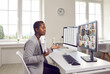 © Studio Romantic - Woman making presentation in online business network meeting. Young black lady sitting at work desk in office, looking at desktop computer screen, showing data sheet and talking to team of colleagues