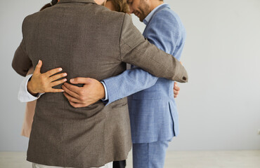 Close up of diverse employees colleagues hug engaged in teambuilding activity in office. Multiracial businesspeople on grey background show unity, have team motivational training at workplace.