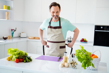 Poster - Photo of cheerful positive man prepare vegetarian meal toothy smile wear apron blue t-shirt home kitchen indoors