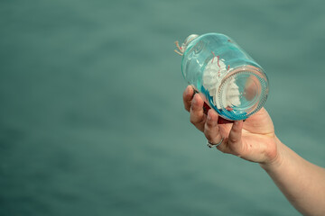 A woman's hand holding a bottle with a small boat inside