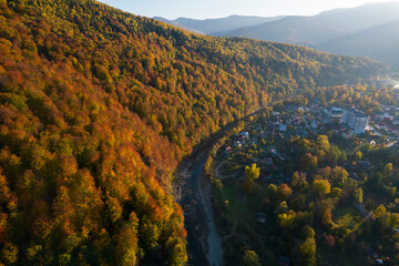 Wall Mural - Top down aerial view of the small village between mountains in autumn. Landscape drone photo of mountains and trees colored into fall colors