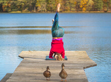 Beautiful Blonde Hair Girl Doing Yoga On A Wooden Pier On The Lake In Autumn With Forest On Background And Ducks