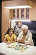 © pressmaster - Happy grandparents sitting at the table in the kitchen and playing board game with their granddaughter