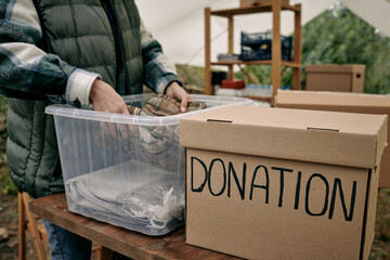 Wall Mural - Female volunteer putting folded clothes into plastic container with donation for homeless people