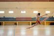 © Albert Martinez/Stocksy - Side view of young rhythmic gymnastics athlete jumping forward with a ribbon