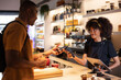 © BONNINSTUDIO/Stocksy - Smiling black waitress taking contactless payment on POS terminal from client