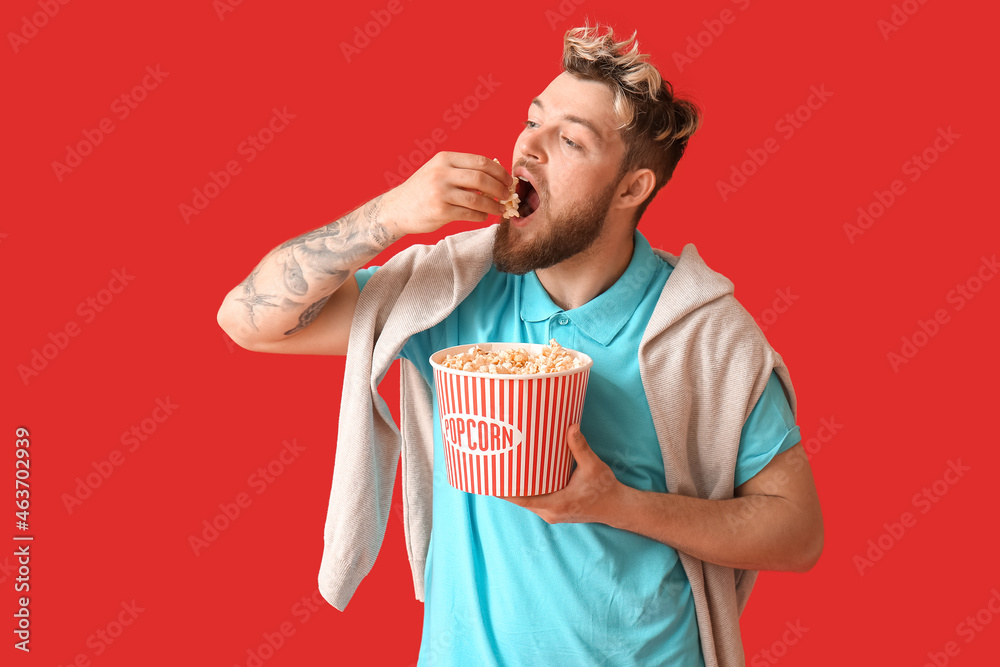 Young guy eating popcorn on color background