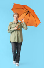 Wall Mural - Young woman with open orange umbrella on blue background