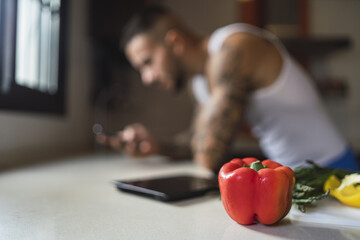 Canvas Print - Closeup shot of a red bell pepper on a kitchen table with a male athlete in the blurry background