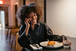 © BONNINSTUDIO/Stocksy - Black woman speaking on smartphone in restaurant