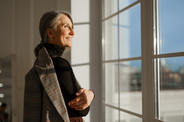 Wall Mural - European senior woman with grey hair smiling while looking out window