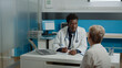 © DC Studio - Doctor with healthcare expertise consulting elder woman sitting at desk in medical office. Young medic in uniform giving advice to sick old patient at hospital facility. People discussing disease