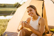 White woman drinking tea while sitting in tent during camping