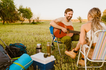 White couple playing guitar while resting during camping together