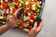 © pundapanda - An adult woman takes pictures of stewed vegetables on the phone for social networks or a culinary blog, top view, home cooking hobby, healthy lifestyle
