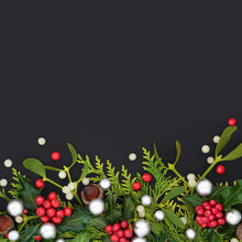 Decorative Christmas Background Border With Silver Baubles, Winter Greenery Of Fir Holly, Cedar Cypress, Mistletoe, Acorns And Ivy Leaves With Red Berries On  Dark Grey . Top View, Copy Space.