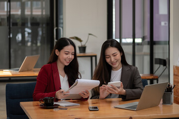 Wall Mural - Two asian female colleagues sitting next to each other in an office, business meeting discussion concept