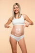 Future mother showing a smiley face drawing on belly on a beige background