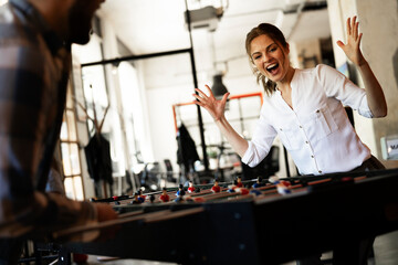 Colleagues having fun at work. Businessman and businesswoman playing table soccer..