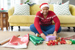 © Wavebreak Media - Happy african american plus size woman in santa hat wrapping presents at home