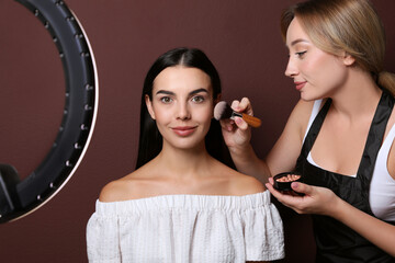 Canvas Print - Professional makeup artist working with beautiful young woman against brown background. Using ring lamp