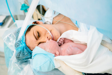 The first moments of mother and newborn after childbirth. Newborn child seconds and minutes after birth. Premature baby boy delivered by Caesarean section, being shown to his mother.