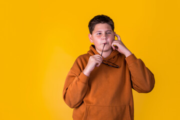 handsome boy with glasses in a brown sweatshirt on a yellow background