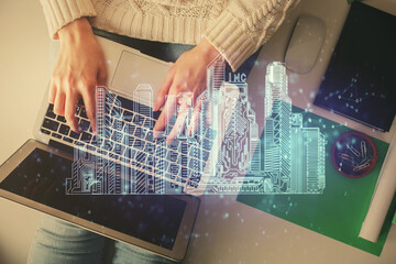 Double exposure of woman hands working on computer and buildings construction hologram drawing. Top View. smart city concept.