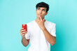 © luismolinero - Young Argentinian man holding a refreshment isolated on blue background having doubts while looking up
