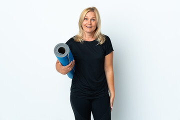 Wall Mural - Middle age woman going to yoga classes while holding a mat isolated on white background with surprise and shocked facial expression