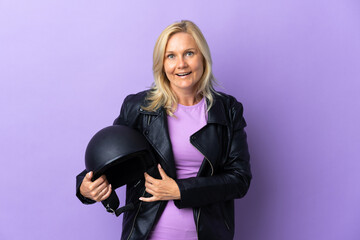 Wall Mural - Middle age woman holding a motorcycle helmet isolated on purple background with surprise facial expression