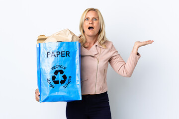 Wall Mural - Middle age woman holding a recycling bag full of paper to recycle isolated on white background with shocked facial expression