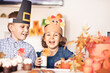 © zulfiska - Kids sitting on festive table and celebrating Thanksgiving day. Children in paper turkey hat and pilgrim hats eating cupcakes and drinking milk.