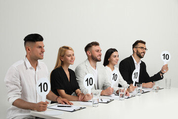 Wall Mural - Panel of judges holding signs with highest score at table on white background