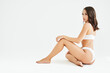 Perfect young woman with sporty body in underwear sitting on floor posing on white studio background