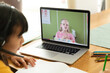 Asian girl using laptop for video call, with caucasian elementary school pupil on screen
