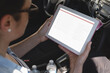 Biracial female programmer sitting in car, holding tablet with copy space on screen
