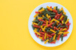 Red green and yellow dry raw fusilli pasta on a plate with yellow background and copy space.