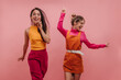 Asian beautiful girl runs forward near caucasian teenager on pink background with place for text. Portrait of two energetic brunettes and blonde models waving hands. Emotions, state of mind concept