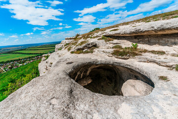 Panoramic view of huge hole in ground among green field and mountain on sunny summer day in Crimea. Abnormal cave, failure in ground. Anomaly grotto.
